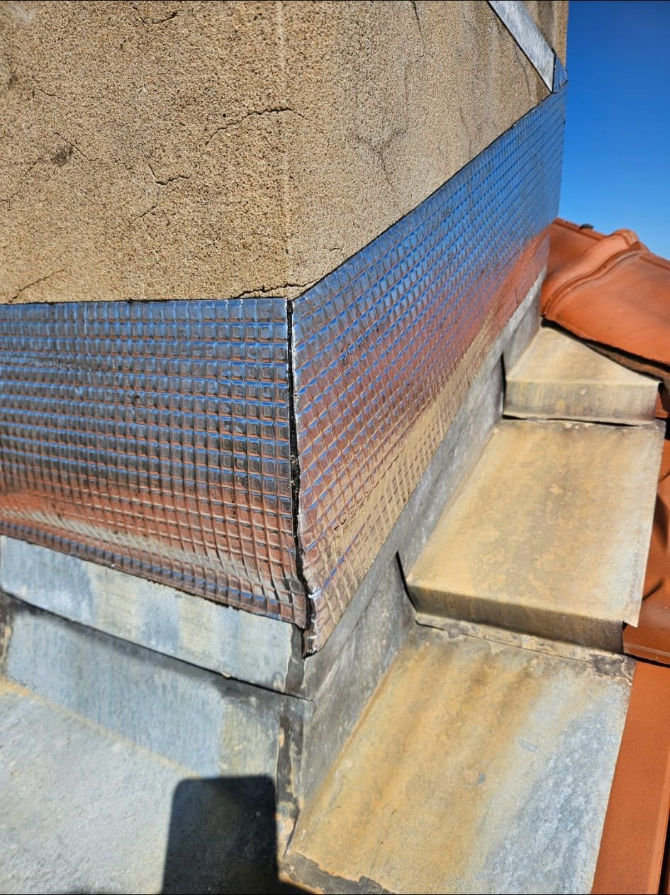 Angle d'une cheminée habillé d'un solin en zinc neuf, au-dessus des tuiles.