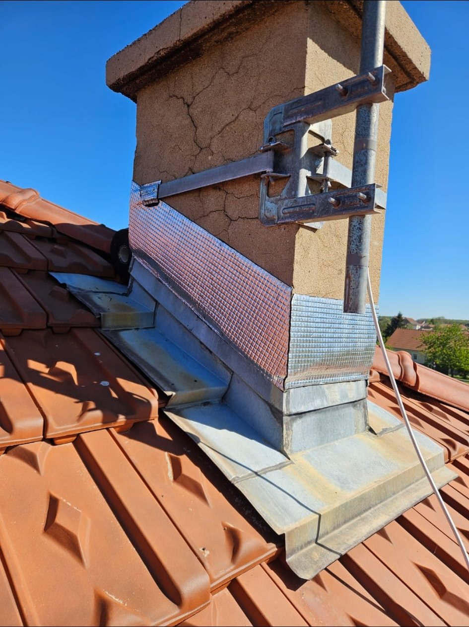 Cheminée sur un toit de tuiles, entourée de solins en zinc neufs.