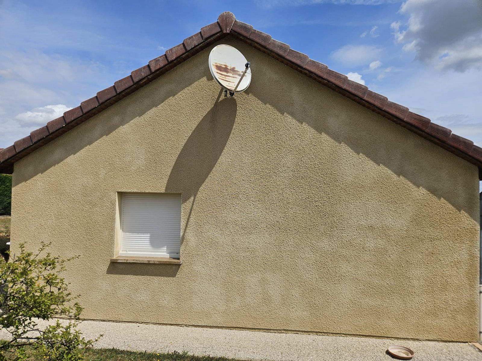 Pignon au crépi beige entièrement nettoyé, sous un ciel bleu.