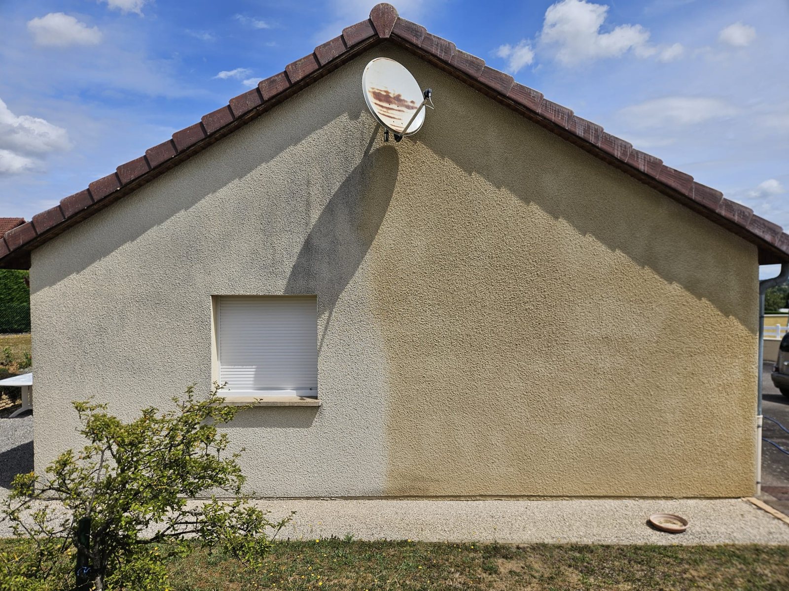 Pignon d'une maison nettoyé à moitié : à gauche le crépi encore gris, à droite le crépi beige retrouvé.